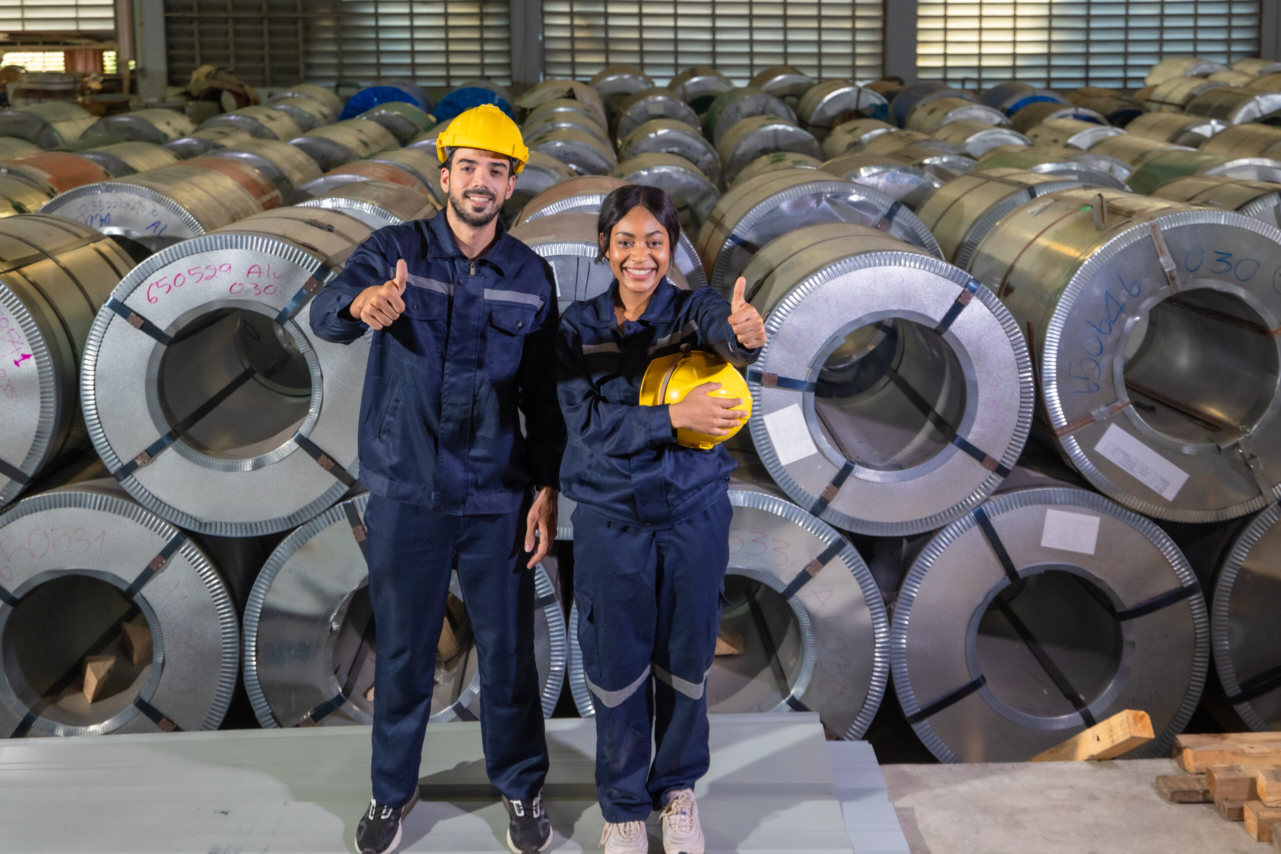 A multicultural group of metal sheet workers proudly give a thumbs up, signaling successful teamwork and job satisfaction in an industrial environment.